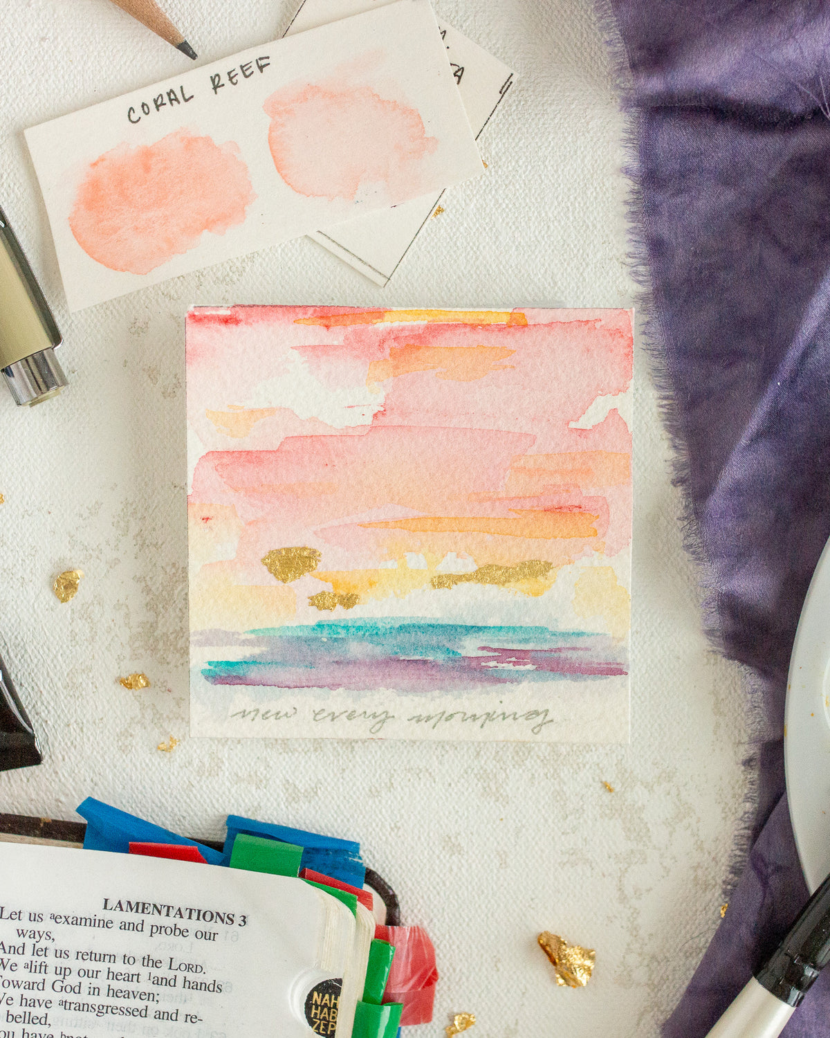Colorful watercolor painting on a textured surface with stationery items.
